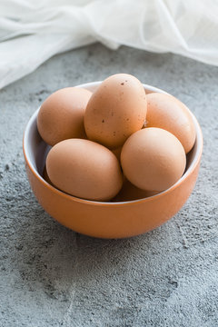Brown chicken eggs in a bowl on a gray stone table..