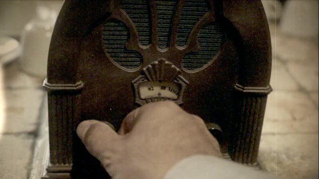 Fake 8mm amateur film: detail close-up of a man's hand turning the dial on an old vintage radio.
