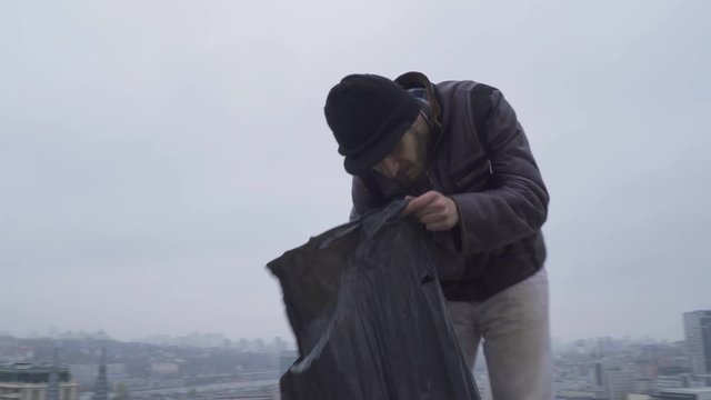 Homeless searches something in the garbage bag at urban background