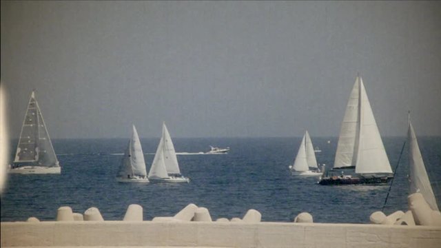 Fake 8mm amateur film: many sailboats at sea, near a pier, in a calm day, getting ready for a regatta.
