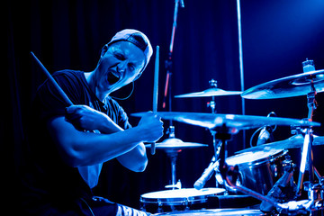 Young drummer posing in front of the camera in a blue concert light