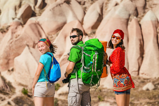 A group of young active and bright travelers walk among the desert colorful hills of tuff in the national park of Cappadocia, Turkey