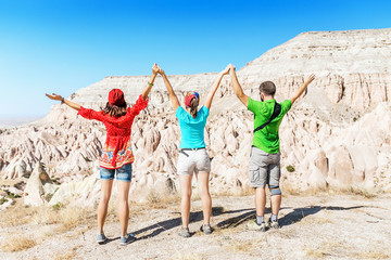 A group of young active and bright travelers walk among the desert colorful hills of tuff in the national park of Cappadocia, Turkey