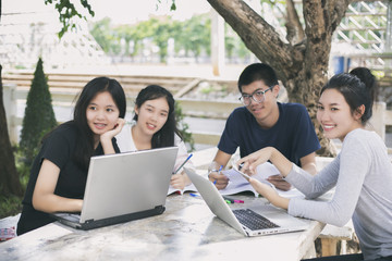 Asian Group of students using tablet and notebook sharing with the ideas for working on the campus lawn