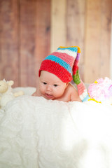 The baby is looking at the camera lying on his stomach in a red striped hat