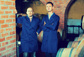 Fototapeta na wymiar two men in uniforms standing in cellar with wine woods