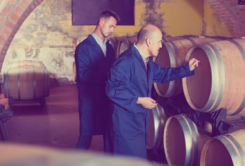 Fototapeta na wymiar two busy men in uniforms taking notes in cellar with wine woods