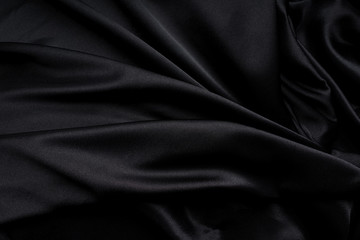 Dark black silky, satin  fabric, wave, draperies. Beautiful textile backdrop. Close-up. Top view 