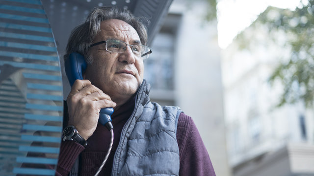  Senior man talking on public payphone in outdoors