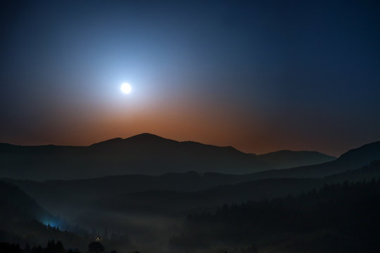 Moon rising above the mountains at night