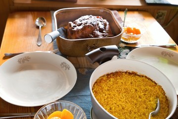 Table with saffron rice in pot, plates, baked chicken and peach compote.