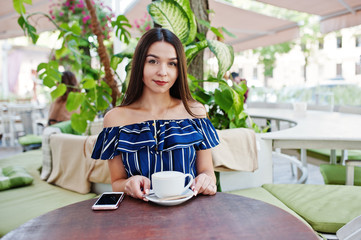 Gorgeous brunette girl sitting on the table in cafe with cup of coffee.