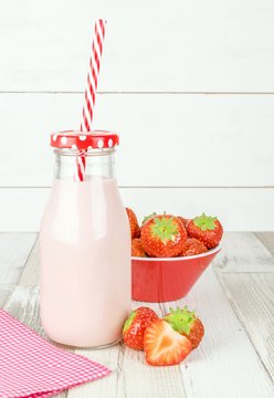 A bottle of strawberry yogurt milkshakes on a wooden table with fresh fruit and copy space