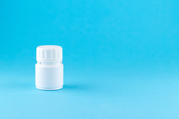 Close up white pill bottle on blue background with copy space. Focus on foreground, soft bokeh. Pharmacy drugstore concept