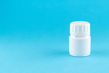 Close up white pill bottle on blue background with copy space. Focus on foreground, soft bokeh. Pharmacy drugstore concept