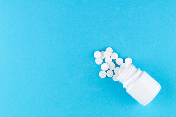 Close up white pill bottle with spilled out pills on blue background with copy space. Focus on foreground, soft bokeh. Pharmacy drugstore concept. Top view