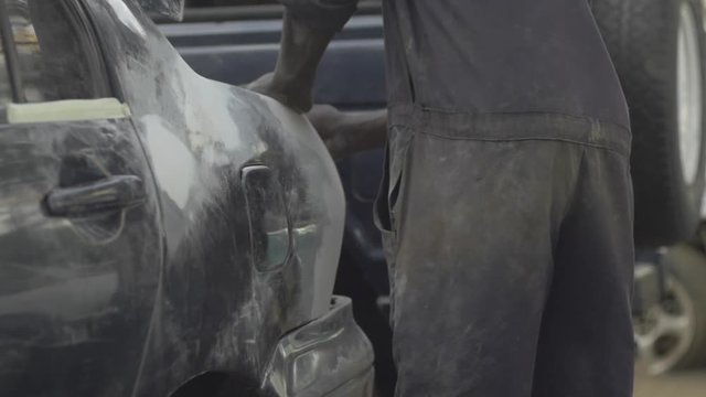 African mechanic sands vehicle, close up, slo-mo.