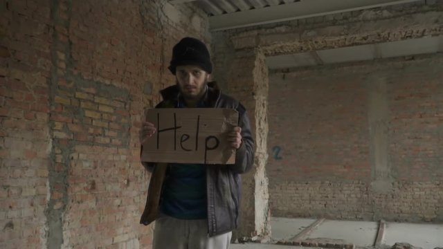 Portrait of sick dirty homeless with table "help"