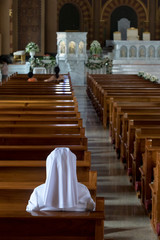The nun sits in the church and prays to God. A nun in traditional white robes meditates in a Christian cathedral. Prayer to Jesus.