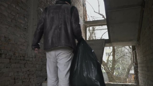 Dirty homeless with garbage bag up stairs in abandoned building
