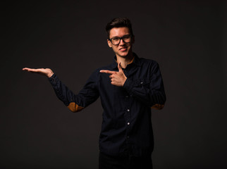 Young jocular man portrait of a confident businessman showing by hands on a black background. Ideal...