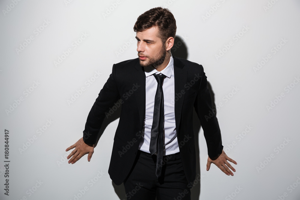 Sticker Handsome businessman in black suit posing and leaning at white wall