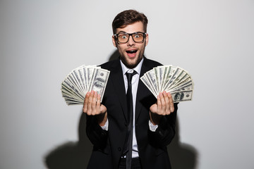 Happy exited man in glasses and black suit holding two bunches of money, looking at camera