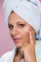 Young woman putting cream on her face