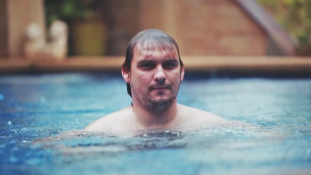 Wet caucasian man gets rained bathing enjoyes while swimming in pool on vacation. 1920x1080