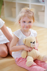 Mädchen spielt mit Teddybar auf Schoß