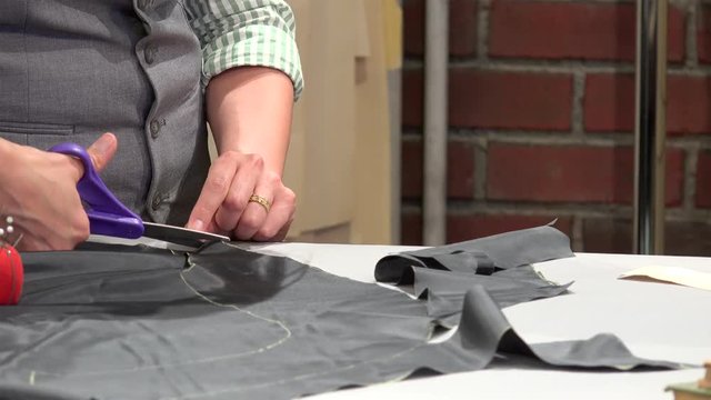 Tailor is cutting a sewing pattern from the grey fabric with scissors.