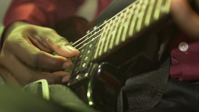 Acoustic six-string guitar. The black man plays the guitar. Club lighting. Very large plan. Macro shooting.