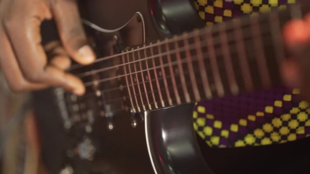 Acoustic six-string guitar. The black man plays the guitar. Club lighting. Very large plan. Macro shooting.