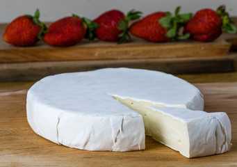 Round of camembert brie cheese with strawberries on the background