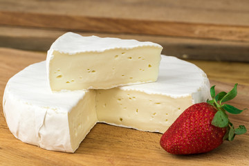 Wheel of Camembert cheese brie with triangle cut out and strawberry.