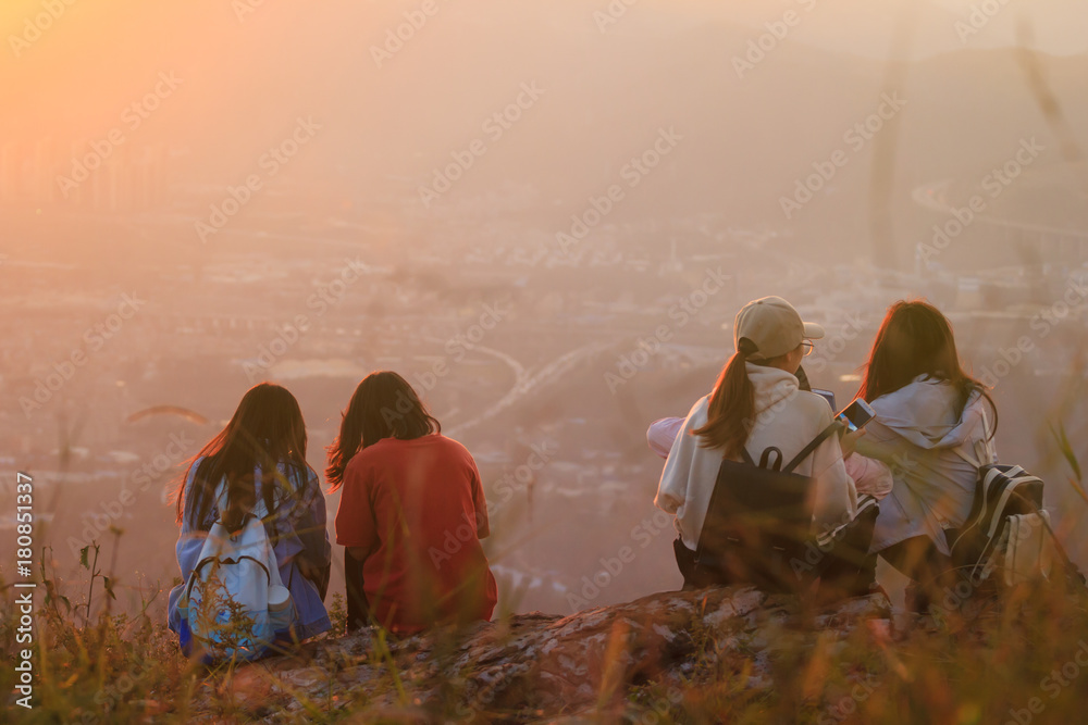 Wall mural Group of girl friends sitting on top of a mountain watching beautiful sunset