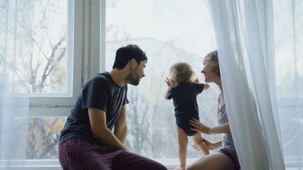 Happy family with young cute daughter sitting on windowsill playing and looking in window at home - Powered by Adobe