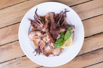 Delicious squids with fresh salad and lemons. Beautiful meal served at the restaurant.