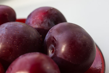 fresh plum fruit in the red saucer on white background
