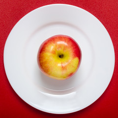 red-yellow apple on a white plate against the red background. square image