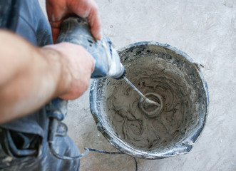 Worker mixing plaster with a drill in a bucket.