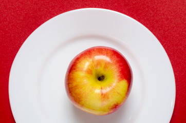 red-yellow apple on a white plate against the red background