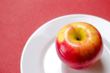 red-yellow apple on a white plate against the red background