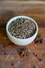 Coriander seeds in bowl on wooden table and spices