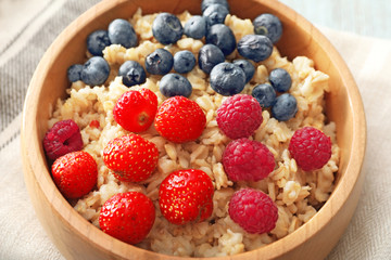 Tasty oatmeal with berries in bowl on table, closeup