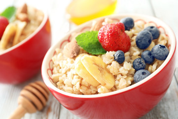 Tasty oatmeal with berries and fruit in bowl on table, closeup