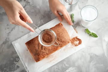 Woman sprinkling powder on delicious cinnamon cake indoors