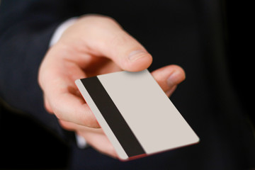Businessmen holding credit card proposing it to you. Hand in black suit holds out a blank grey credit card. Close up