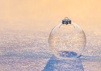 Christmas transparent glass ball with snowflakes on sunset snow surface