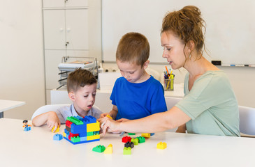 teacher woman play with two child boy with cubes in the kindergarten